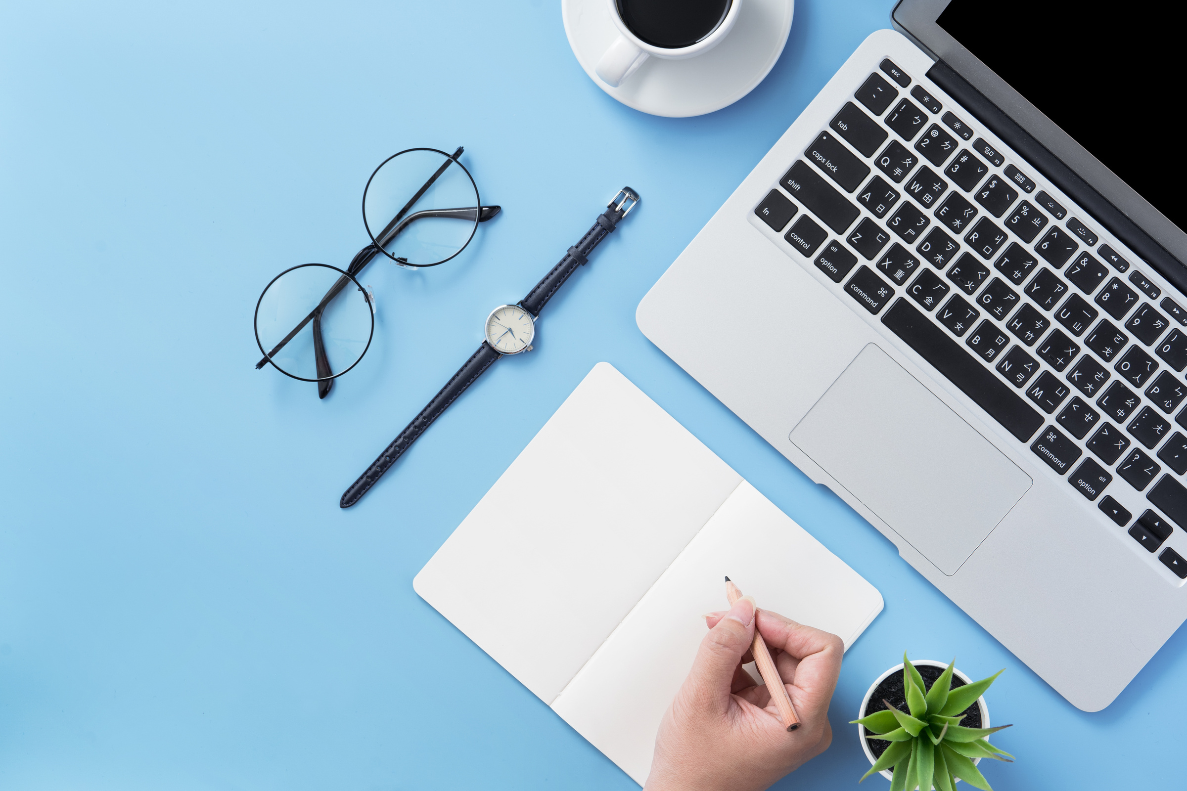 Hand on Open White Book with Laptop on Blue Desk